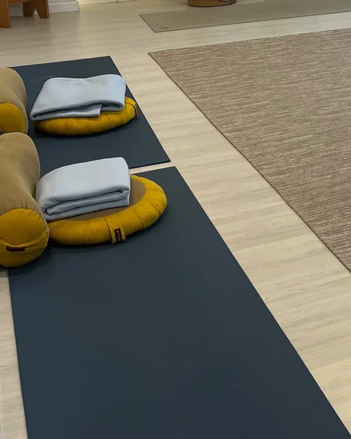 Detalhe da sala: almofadas amarelas com mantas azul-claras dobradas sobre colchonetes escuros, ao lado do tapete